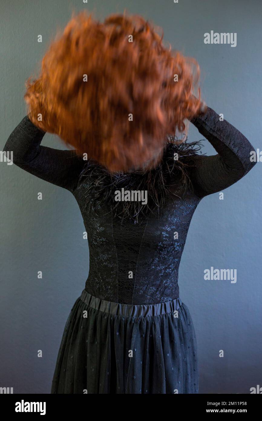 Eine schwarz gekleidete Frau wirft ihr Kastanienhaar zurück Stockfoto