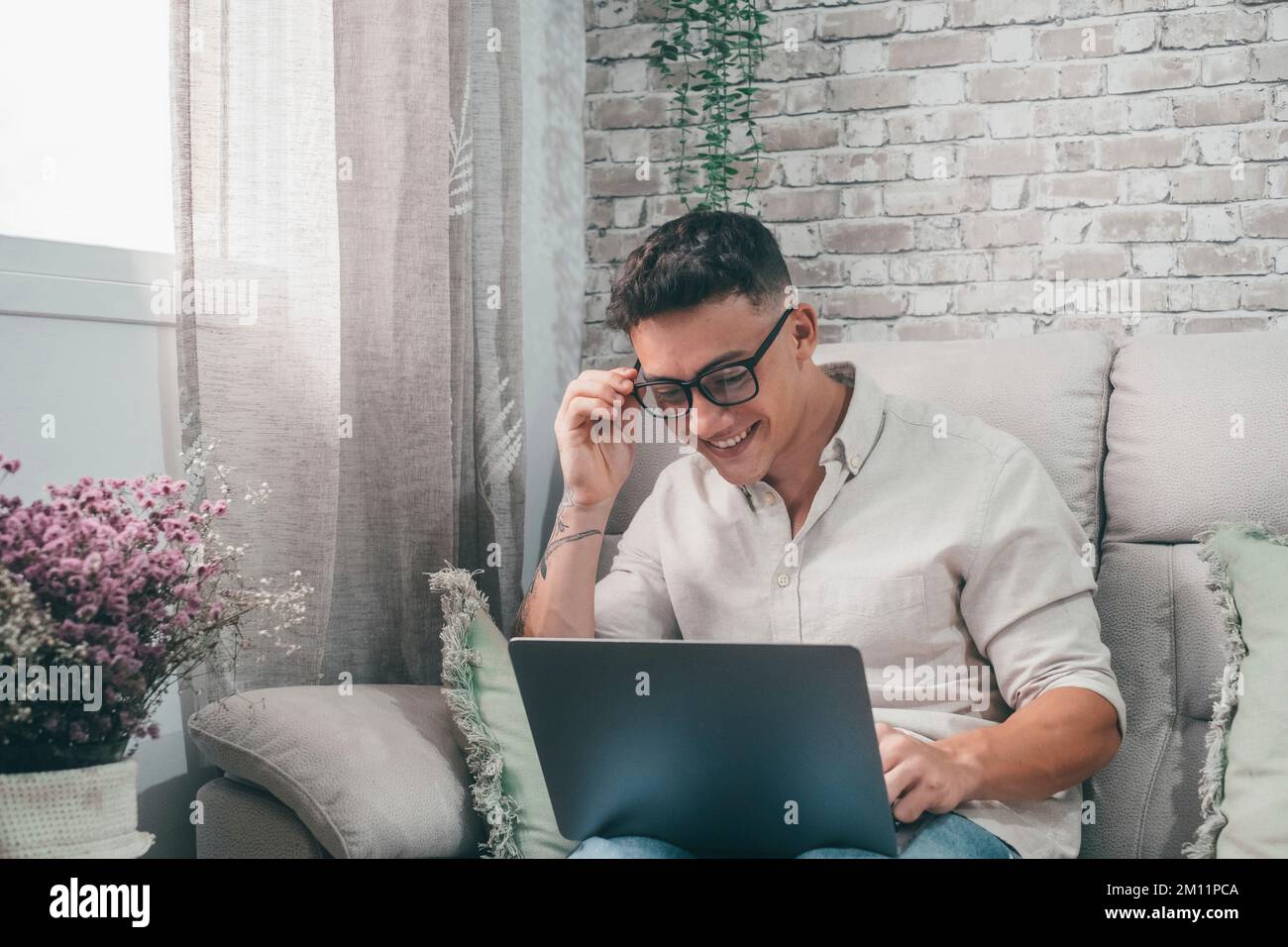 Ein junger glücklicher Mann surfte mit seinem Laptop zu Hause im Internet, sitzt auf dem Sofa und genießt seine Freizeit und entspannt allein. Unternehmer-Junge, der arbeitet und seine Zukunft baut. Stockfoto