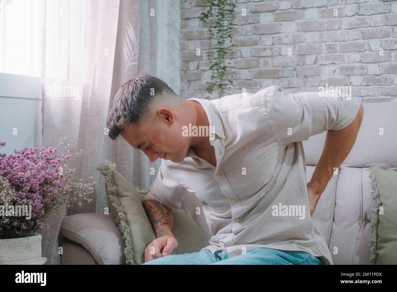 Ein junger Mann, der allein zu Hause unter Rückenschmerzen leidet. Gestresster Teenager, der sich wegen einer Entzündung schlecht fühlt. Stockfoto