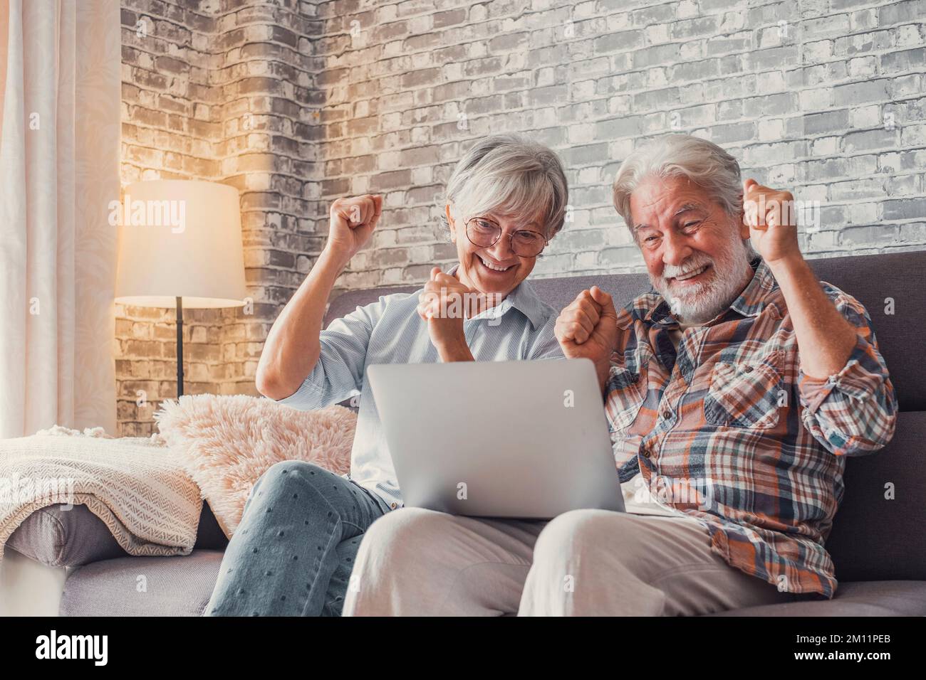 Ein altes Paar reagiert auf ein unerwartetes neues auf seinem Laptop. Zusammen zu Hause genießen. Stockfoto