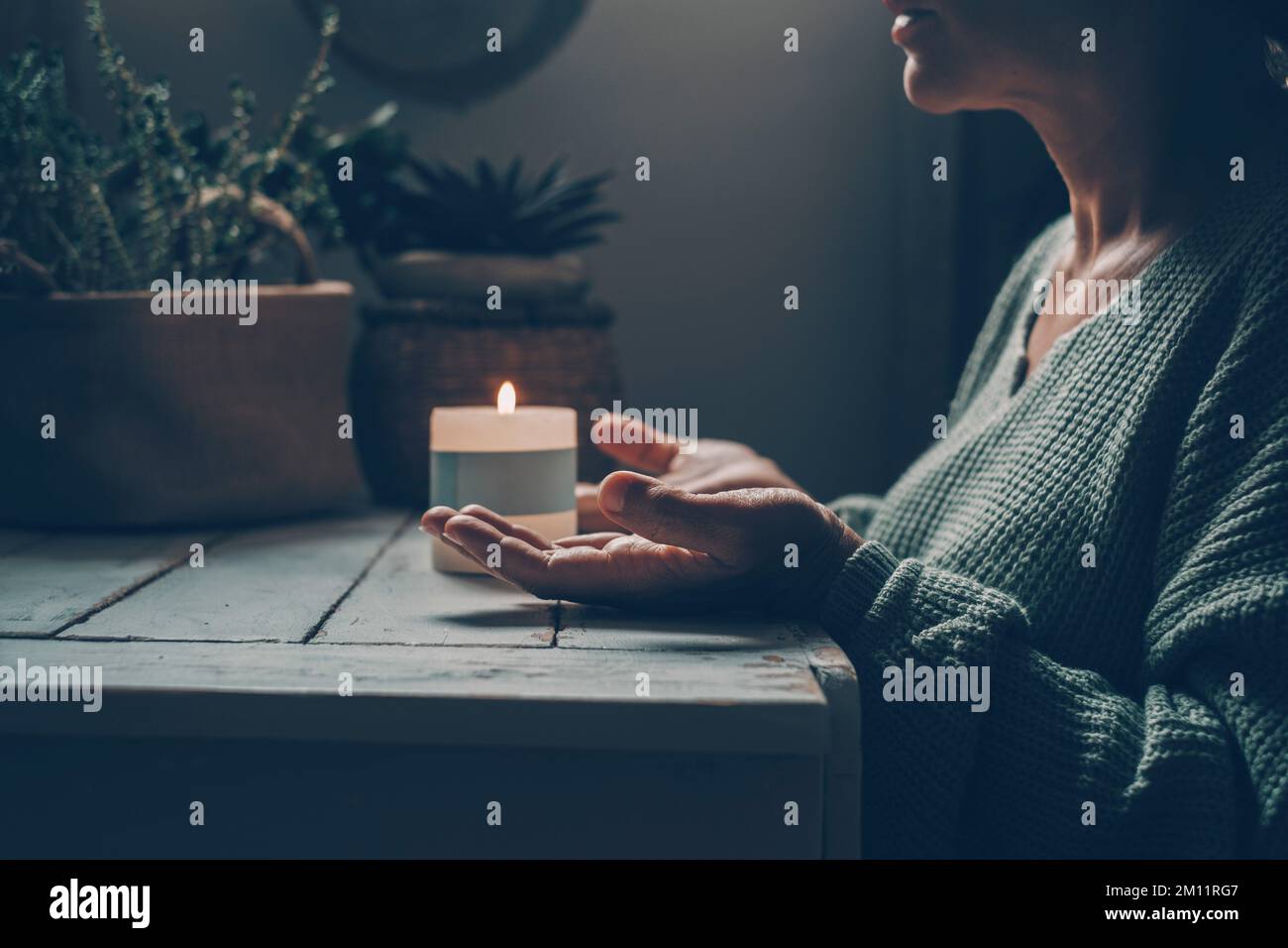 Frau zu Hause bei Zen-Meditationsaktivität und Kerzenlicht im Hintergrund. Eine weibliche Person mit erhobenen Händen betet oder meditiert allein im dunklen Licht drinnen. Konzept einer gesunden psychischen Lebensweise. Die Natur Stockfoto