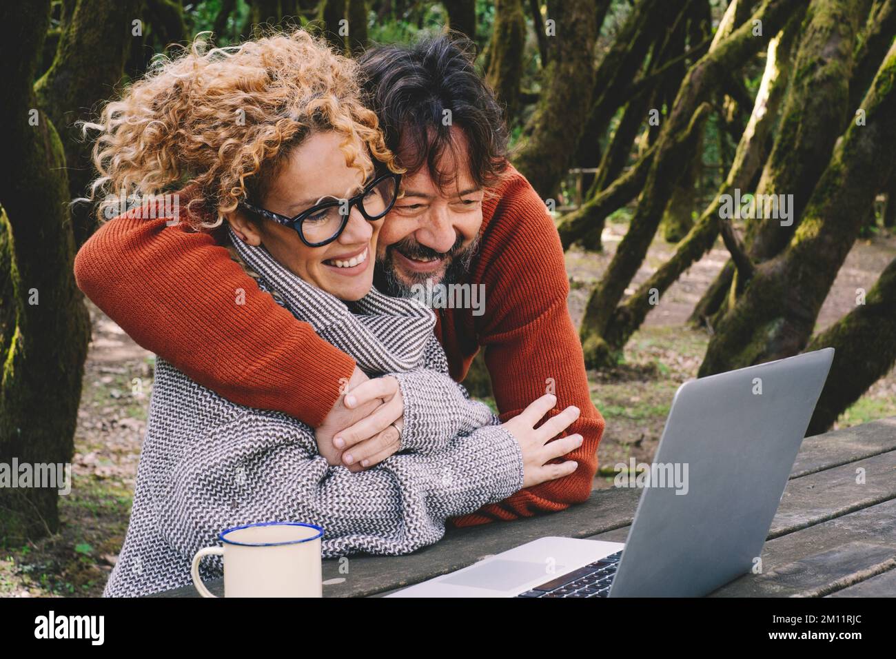 Glückliches Paar in Liebe und Freundschaft Genießen Sie Videogespräche auf einem Laptop, umarmen und lächeln Sie zusammen. Natur im Freien Waldlandschaft. Konzept der Nutzung von Computern überall. Reisen Sie moderne Abenteurer Stockfoto