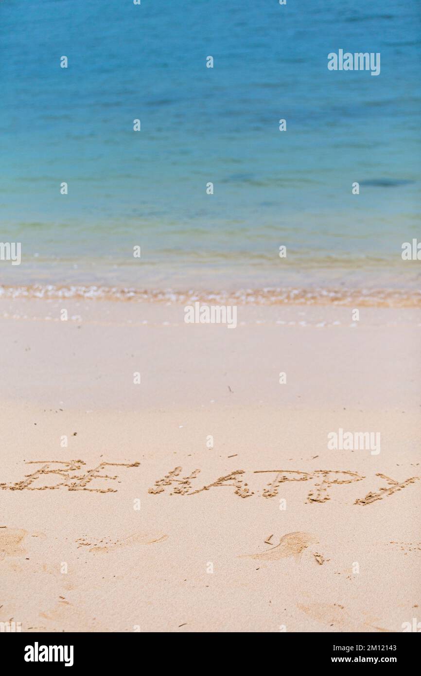 Seien Sie glücklich - wie eine Nachricht mit einem Finger im Sand geschrieben an einem Strand mit Wellen und blauem Ozean auf Mauritius Island, Afrika, Draufsicht, niemand Stockfoto