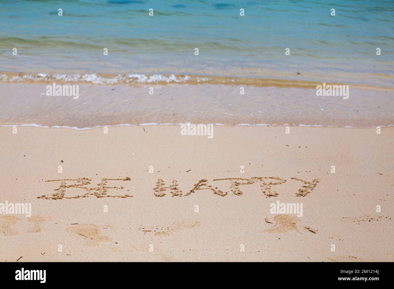 Seien Sie glücklich - wie eine Nachricht mit einem Finger im Sand geschrieben an einem Strand mit Wellen und blauem Ozean auf Mauritius Island, Afrika, Draufsicht, niemand Stockfoto