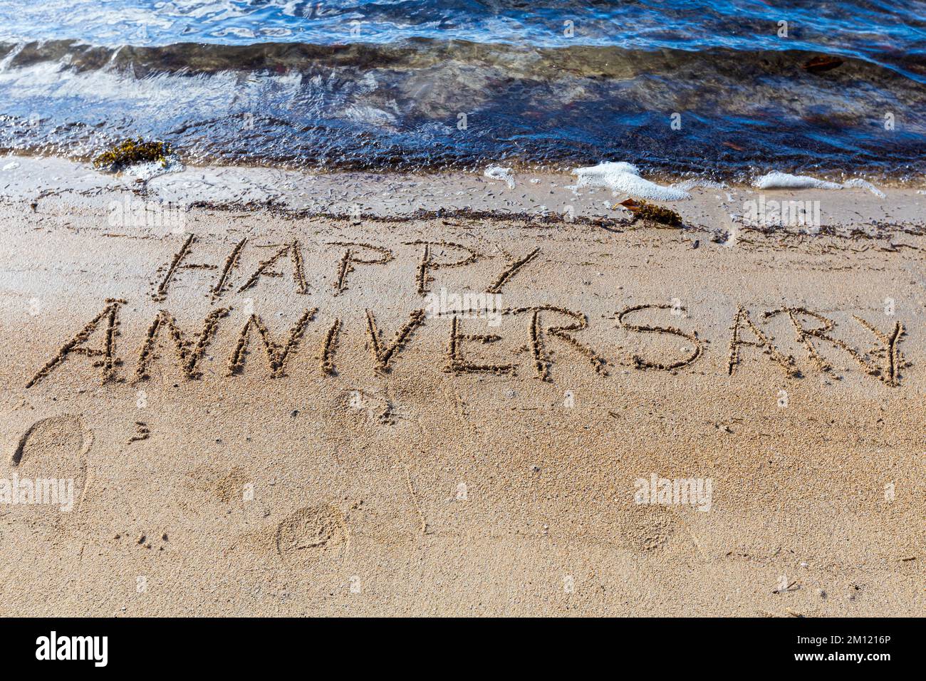 Happy Anniversary - wie eine Nachricht geschrieben mit einem Finger im Sand an einem Strand mit Wellen und blauem Ozean auf Mauritius Island, Afrika, Draufsicht, niemand Stockfoto