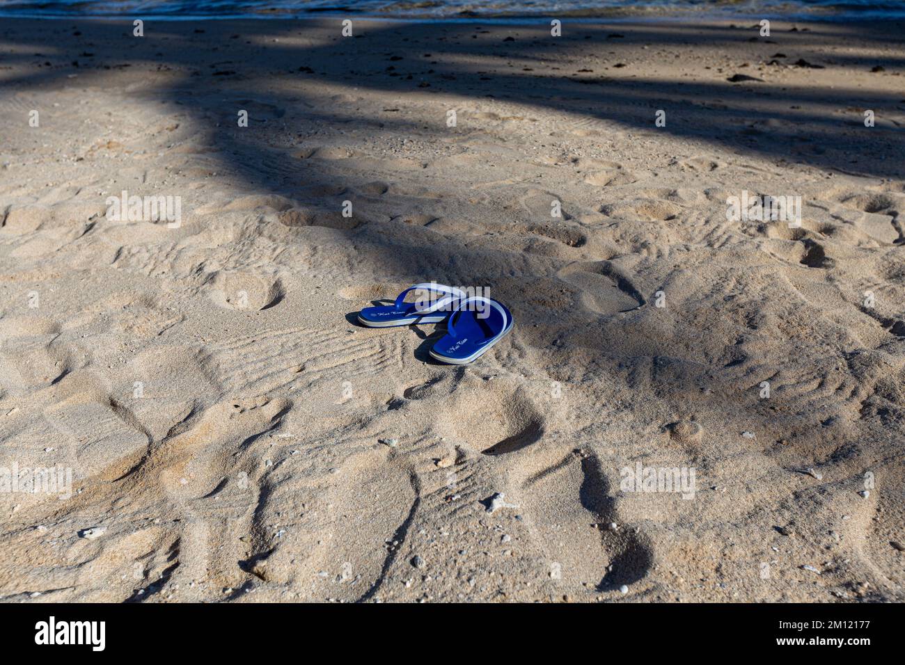 Flip-Flops oder Sandalen für Frauen am Sandstrand an der Küste mit Effekt, dass die Sonne auf dem Meer untergeht. Tourismus Entspannen Reisen Sie im tropischen Sommer im Urlaub oder das Konzept des gebrochenen Herzens. Bild mit freiem Speicherplatz. Stockfoto
