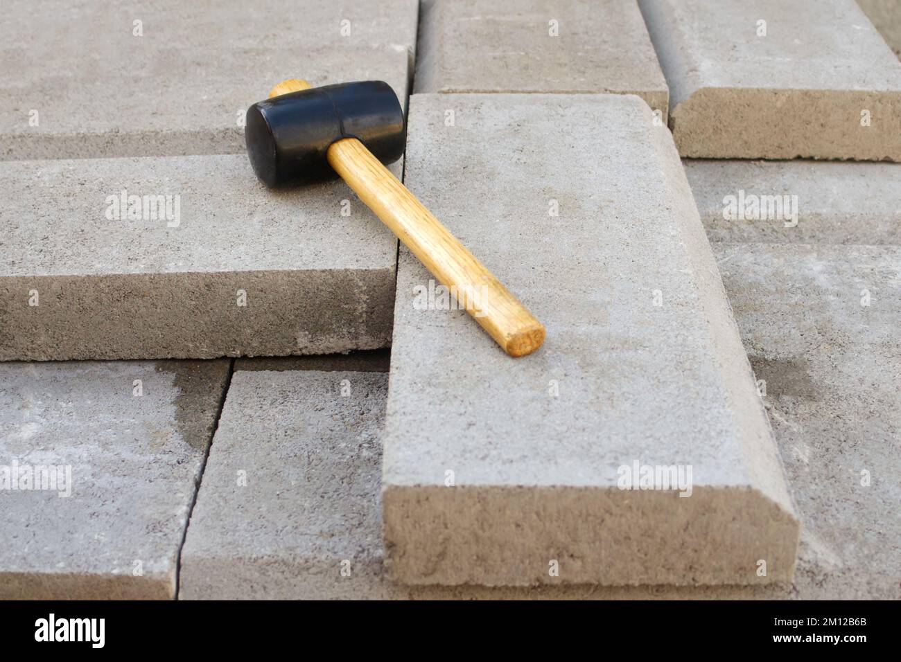 Unschärfe-Pflasterhammer. Stapel Pflastersteine. Pflasterarbeiten auf Backsteinpflastern durch einen professionellen Deckenfertiger. Verlegen von grauen Betonplatten Stockfoto