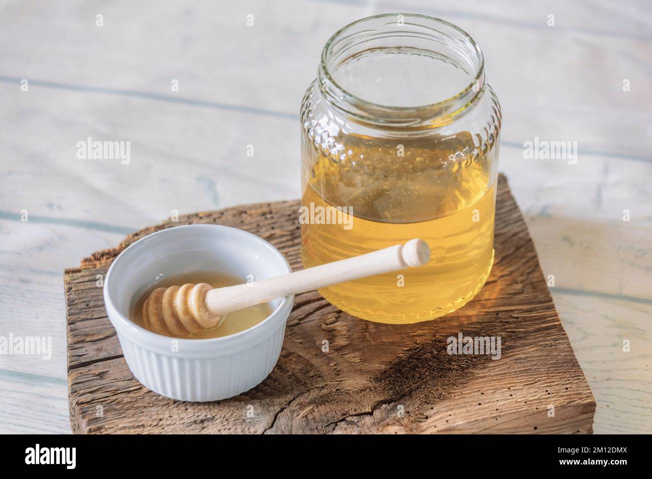 Glasbecher mit Bienenhonig mit kleinem Becher und Honigstiel auf antikem Holzbrett Stockfoto