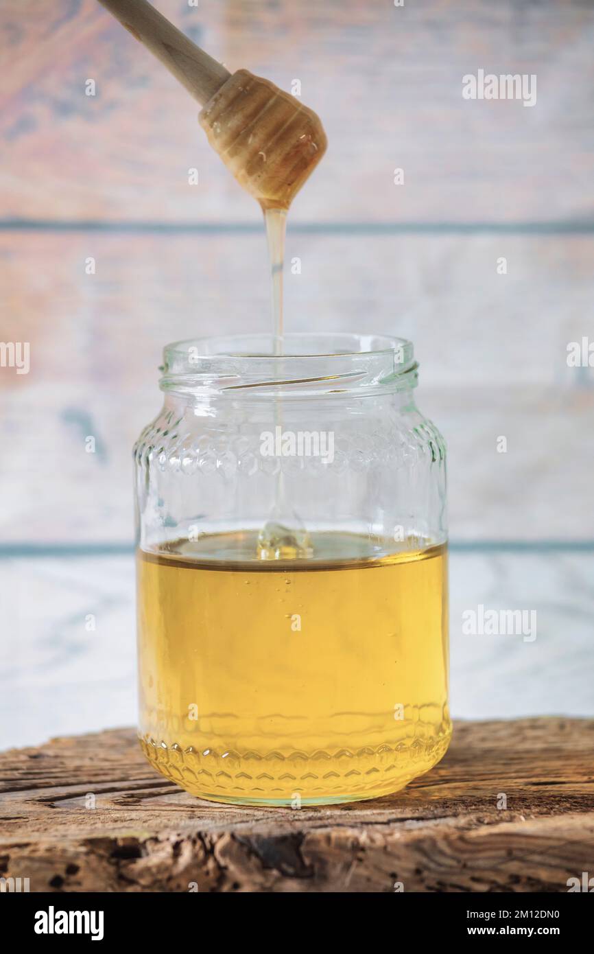 Glas Bienenhonig mit Honigstiel auf antikem Holzbrett Stockfoto