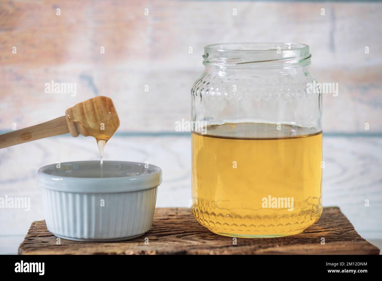 Glas Bienenhonig mit kleinem Becher und Honigstiel auf antikem Holzbrett Stockfoto