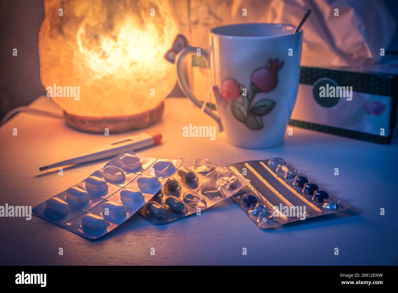 Nachttisch beleuchtet von einer Salzlampe, mit Medikamenten und Fieberthermometer Stockfoto