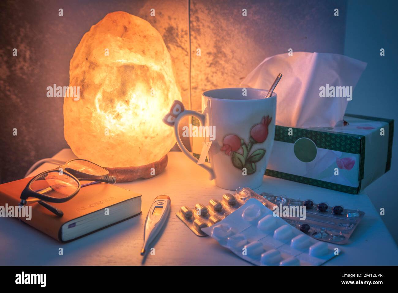 Nachttisch beleuchtet von einer Salzlampe, mit Medikamenten und Fieberthermometer Stockfoto