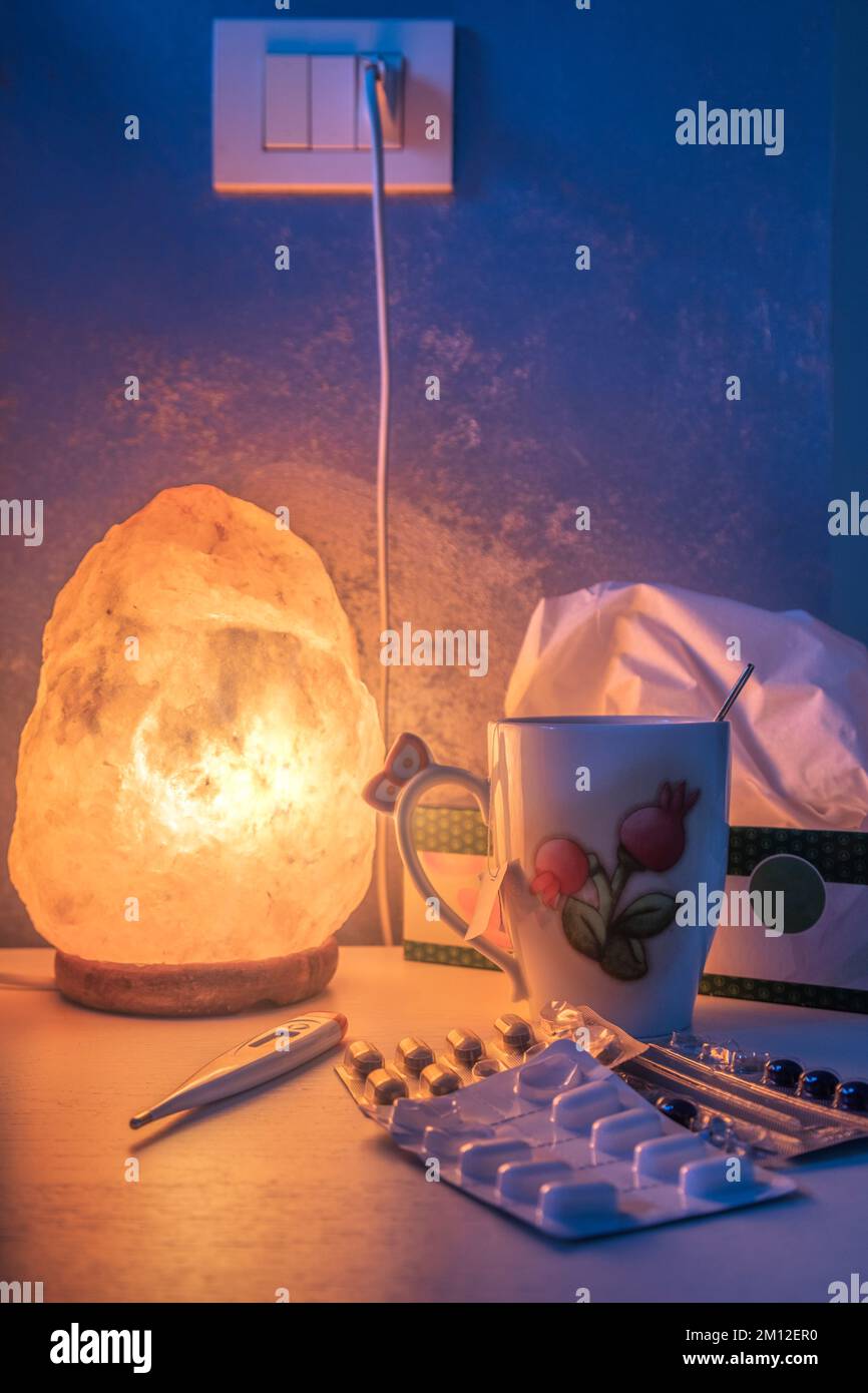 Nachttisch beleuchtet von einer Salzlampe, mit Medikamenten und Fieberthermometer Stockfoto