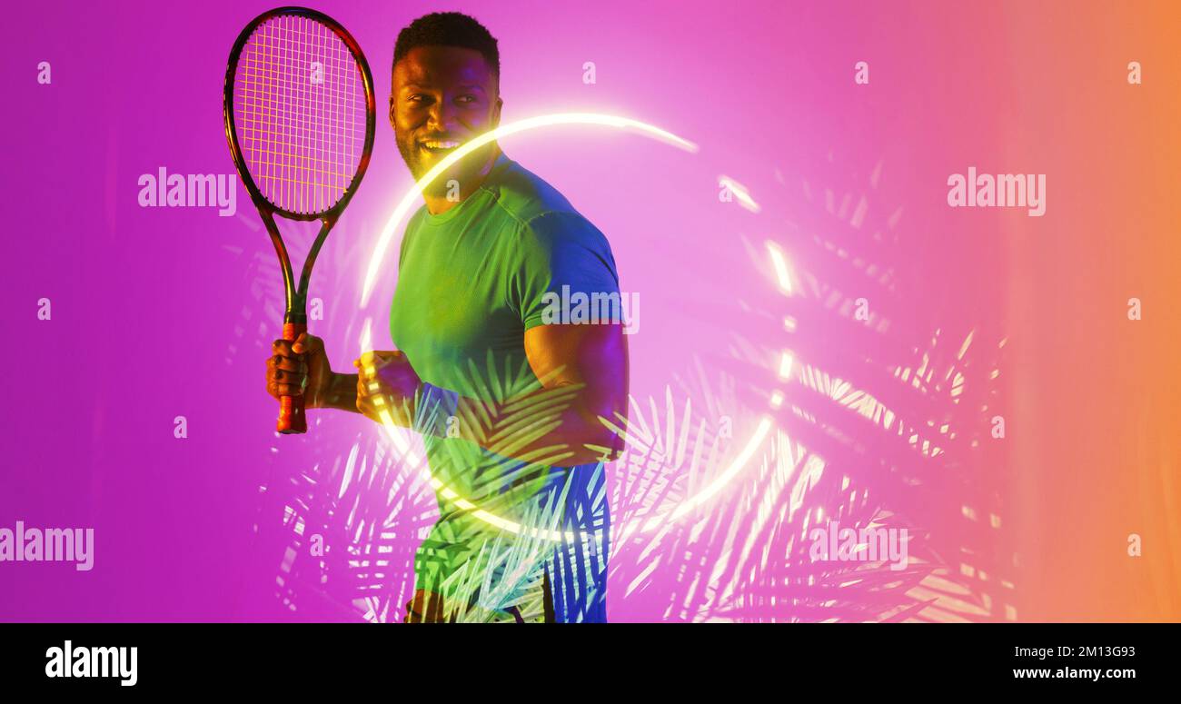 Ein glücklicher afroamerikanischer Tennisspieler hält einen Schläger an beleuchteten Pflanzen und einem Kreis Stockfoto