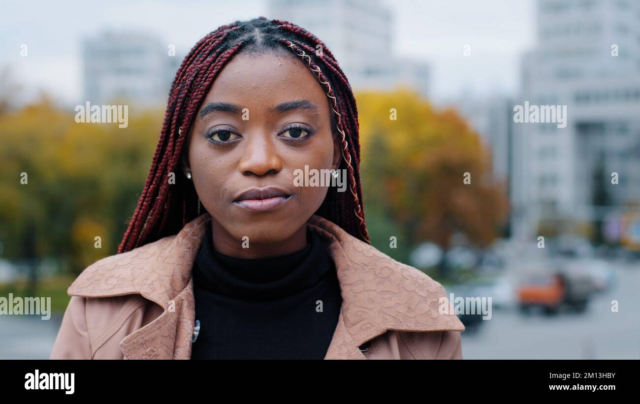 Weibliches Porträt Nahaufnahme junge, ernsthaft pensive, schöne, schicke afroamerikanische Frau, die draußen steht und die Kamera ansieht frustrierte, ethnische Aufregung Stockfoto