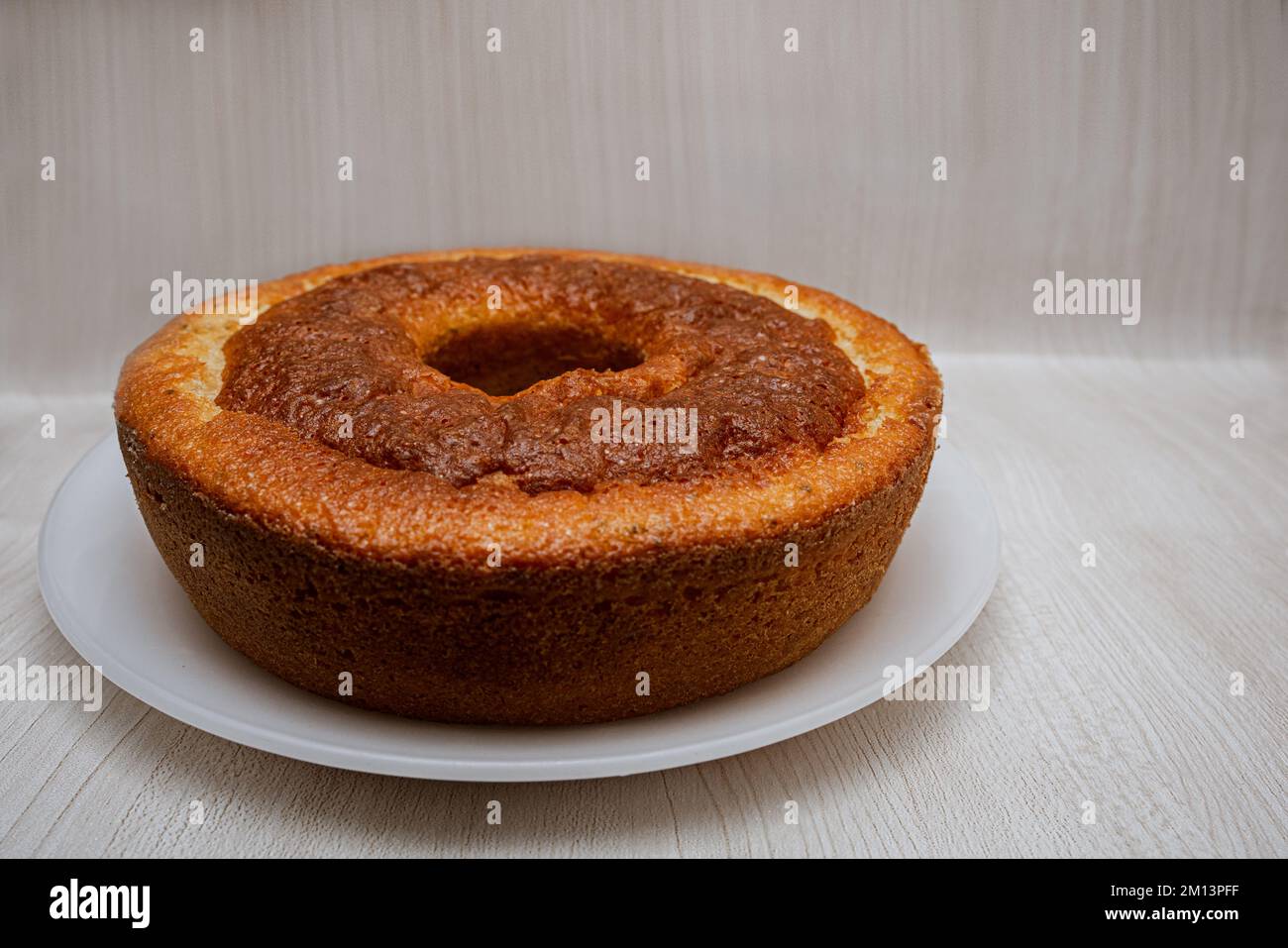 Ein frisch gebackener hausgemachter Rundkuchen mit einem Loch in der Mitte auf einem Gericht, isoliert auf hellem Hintergrund und leerem Platz für Text. Traditioneller Kuchen Stockfoto