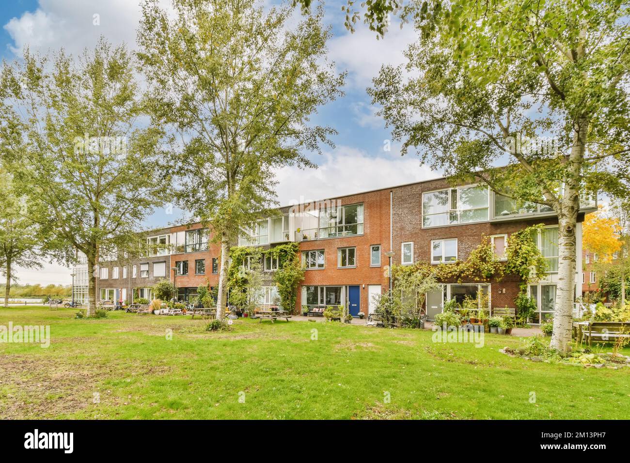 Ein Apartmentkomplex mit Bäumen im Vordergrund und Gras auf dem Boden, umgeben von üppig grünen Rasen unter blauem Himmel Stockfoto