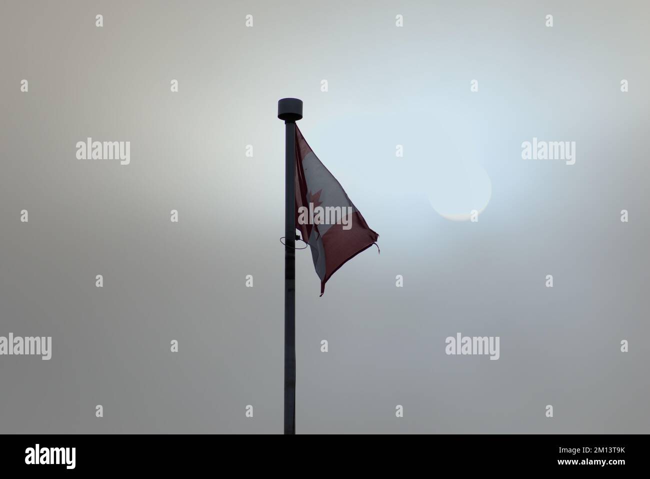 Kanadische Flagge an einem nebeligen Morgen mit einer sehr hellen Sonne dahinter. Stockfoto