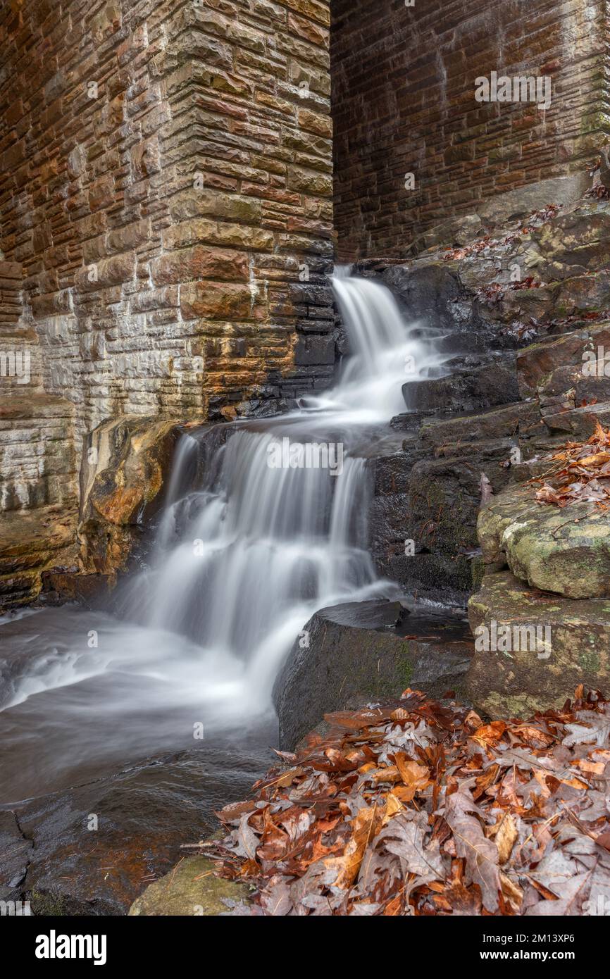 Ein kleiner Auslauf am Byrd Creek Dam in Cumberland Mountain, Tennessee, zeigt die Herbstfarben und Ziegeldetails, während das Wasser hinunter zum riv fließt Stockfoto