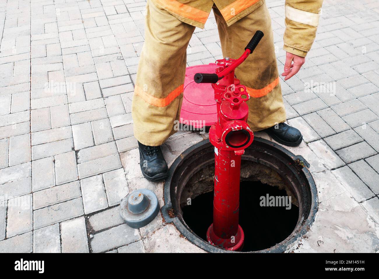 Feuerwehrmann oder Retter installiert Hydranten im offenen Brunnen. Feuerwehrarbeit im Brandfall. Schulung und praktische Übungen im Brandfall. Hintergrund... Stockfoto