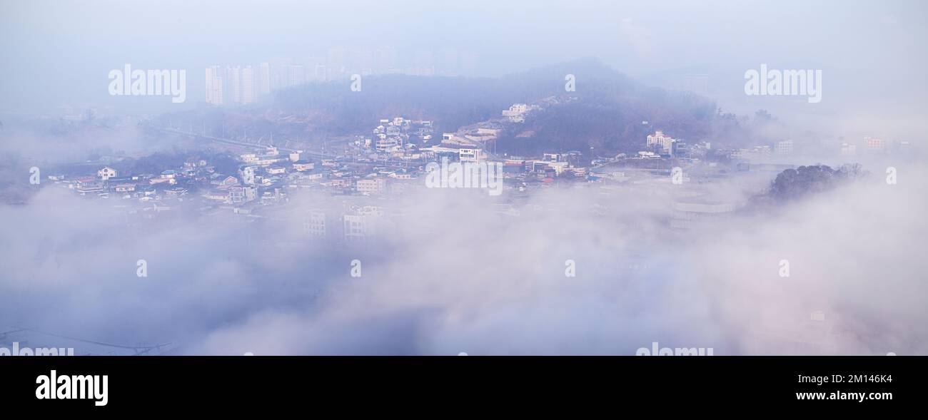 Ein atmosphärischer Blick auf eine moderne Skyline der Stadt, die teilweise von dichtem Morgennebel verdeckt wird, schafft eine geheimnisvolle und stimmungsvolle Stadtlandschaft. Stockfoto