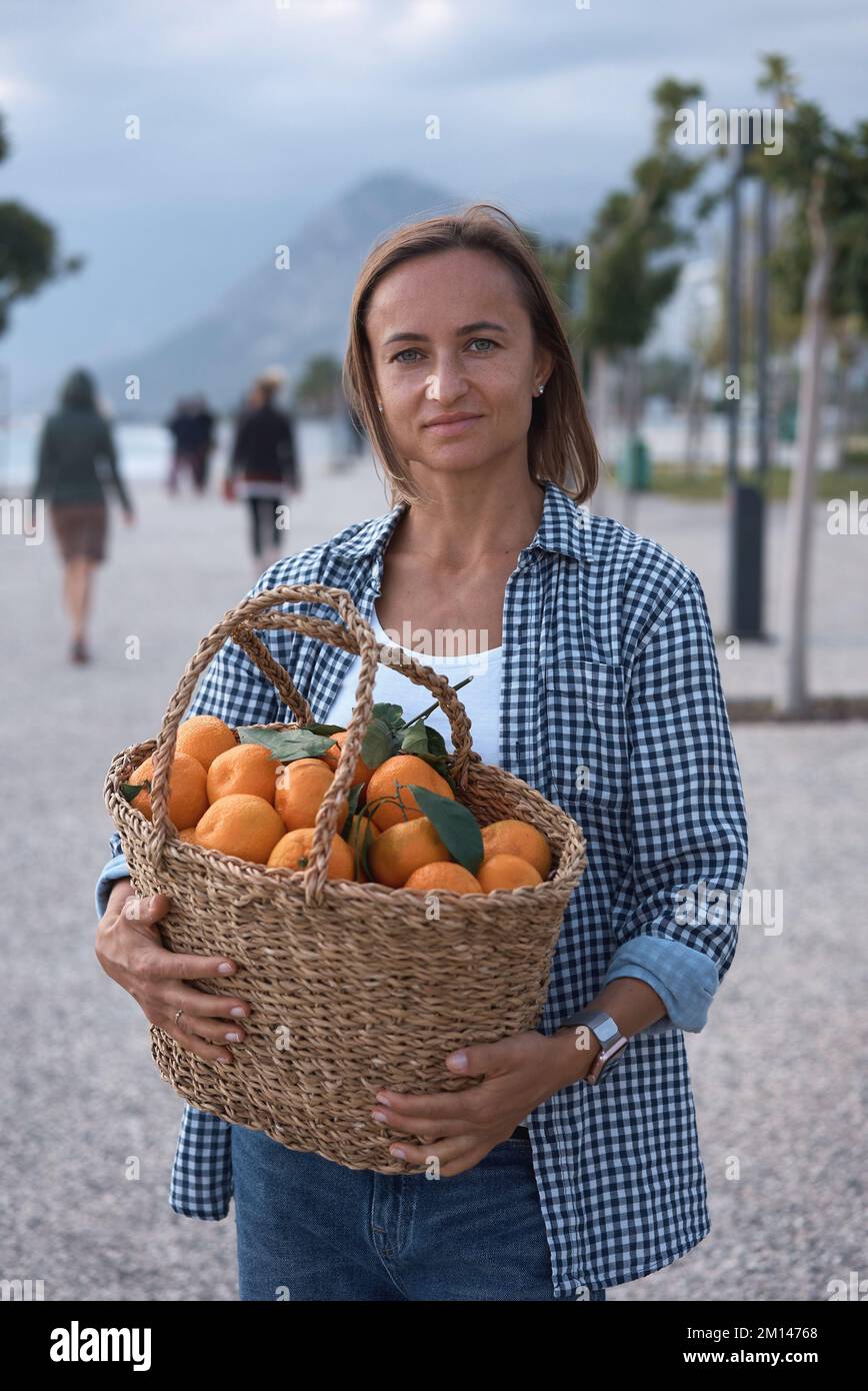Eine Frau, die einen Korb voller Obstmandarin hält. Mandarinsaison Stockfoto
