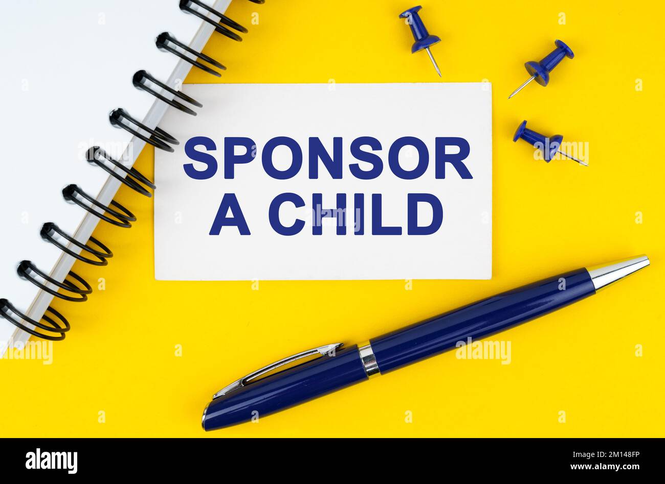 Geschäfts- und Finanzkonzept. Auf gelbem Hintergrund befinden sich ein Notizbuch, ein Stift und eine Visitenkarte mit der Aufschrift „Sponsor A Child“ Stockfoto
