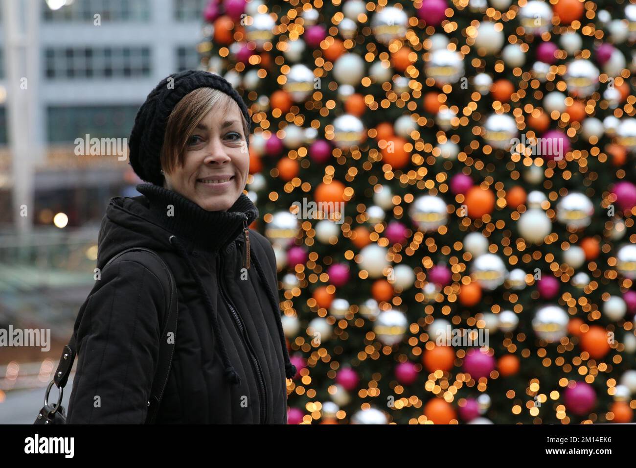 Die beste Weihnachtszeit für das ältere Modell am großen Weihnachtsbaum mit einem Lächeln im Gesicht. Frau im besten Alter steht vor einem großen Weihnachtsbaum glücklich Stockfoto