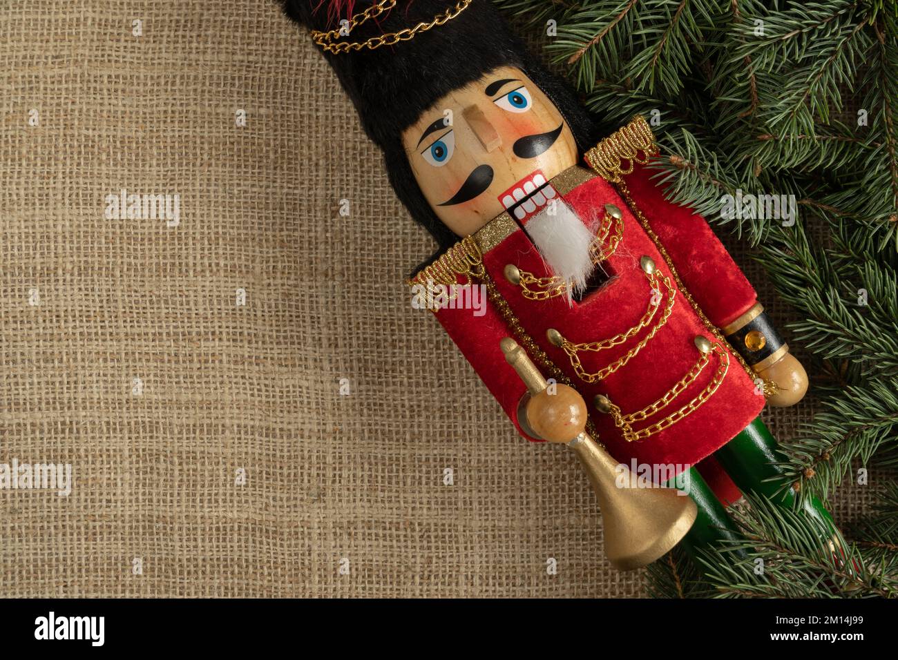Weihnachtsnussknacker Holzfigur und Baumzweige. Festliches Spielzeug mit Soldatendekoration. Flache Laienzusammensetzung mit Kopierraum auf Jutestoff. Stockfoto