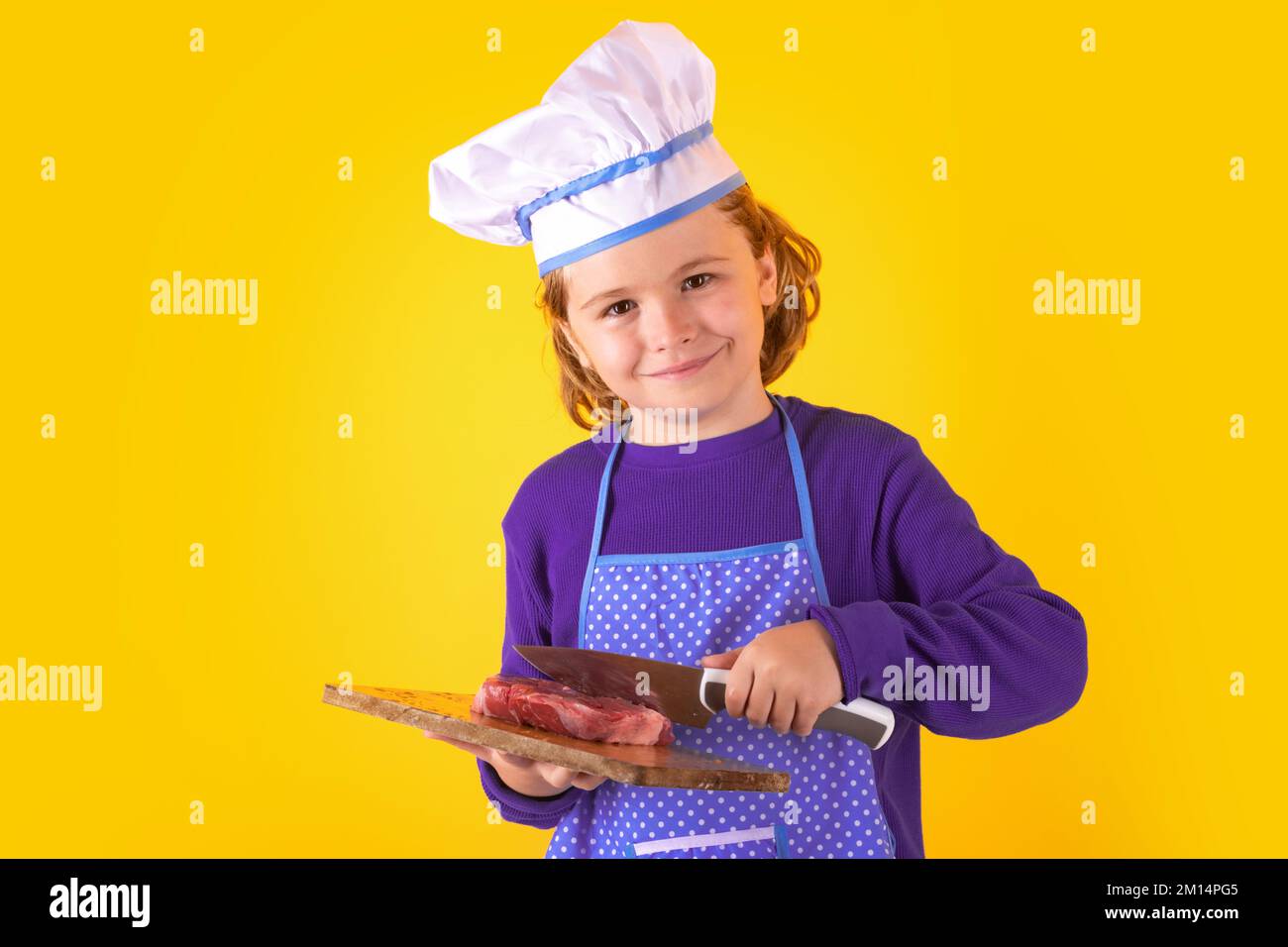 Der Kinderkoch hält das Schneidebrett mit Fleischsteak und Messer. Kinderkoch. Kindergarderobe und Kochmütze für die Zubereitung von Speisen, Studioporträt Stockfoto