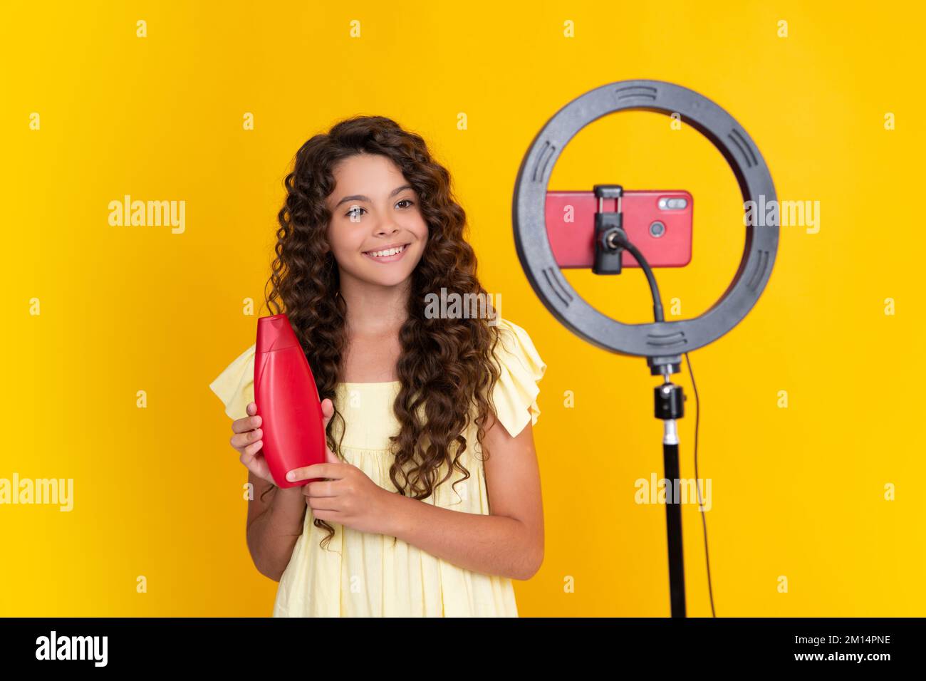 Bloggen, Videoblog. Kinder-Blogger halten Haarspülmittel oder Shampooflasche mit Videoaufzeichnung auf isoliertem gelbem Studiohintergrund Stockfoto