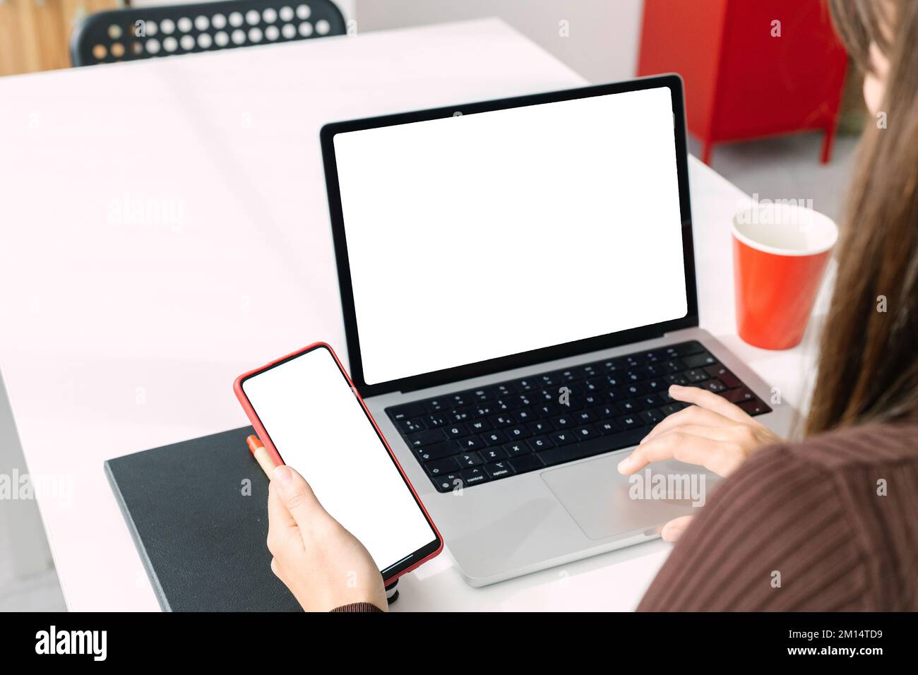 Modellbild eines jungen Menschen, der mit Laptop und Telefon arbeitet, mit weißem, leerem Bildschirm Stockfoto