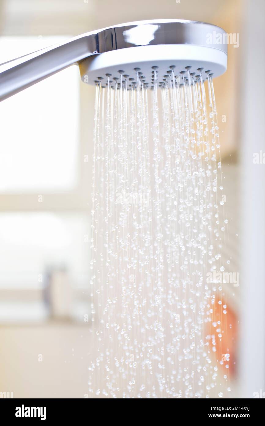 Nahaufnahme von fließenden Wassertropfen aus einem Duschkopf in einem hellen Badezimmer mit Fenster im Hintergrund Stockfoto