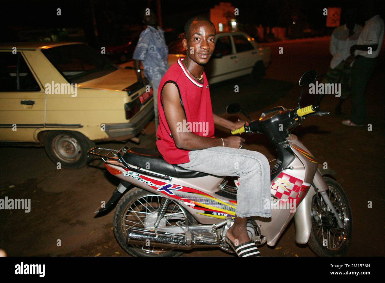 Junger afrikanischer Mann, der auf seinem Motorroller in den Straßen von Malis Hauptstadt Bamako sitzt. Stockfoto