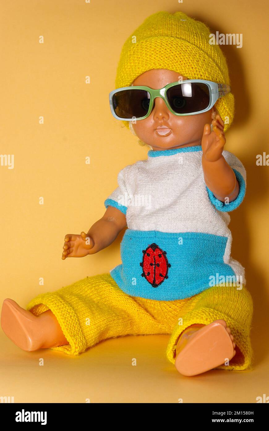 Schicke Puppe mit Sonnenbrille und gelber Strickmütze, Kinderspielzeug aus der DDR der 1970er, Konzept des kindlichen Spielens und des menschlichen Ausdrucks. Stockfoto