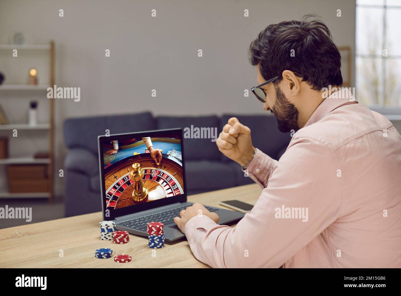 Glücklicher, aufgeregter junger Mann nutzt Laptop, um auf der Internetseite des Online-Casinos zu spielen Stockfoto