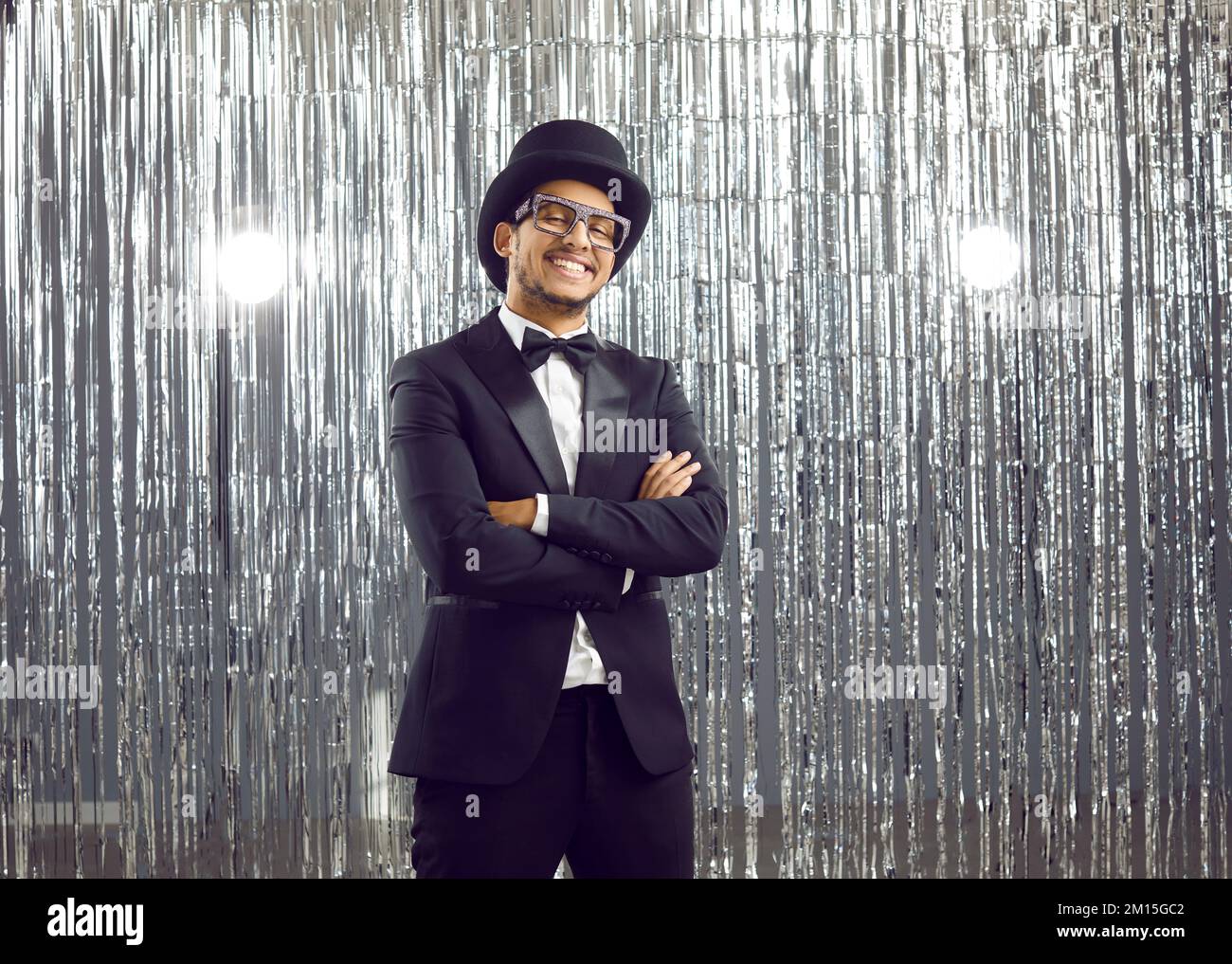 Ein cooler junger, positiver afroamerikanischer Mann im klassischen, eleganten schwarzen Anzug auf silbernem, glänzendem Hintergrund. Stockfoto