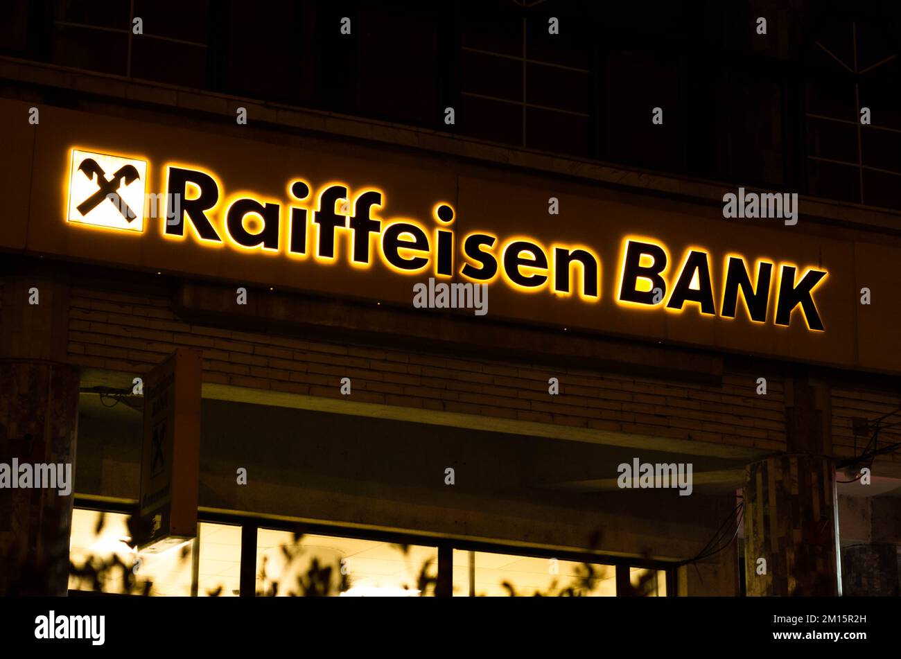 Bukarest, Rumänien - 10. Dezember 2022: Schild und Logo der österreichischen Bank Raiffeisenbank Bank am Abend auf der Straße in Bukarest Stockfoto