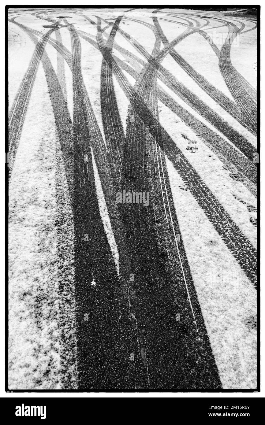 Abstrakte Muster von Reifenspuren, die auf einer Abdeckung mit leichtem Winterschnee gemacht wurden. Stockfoto