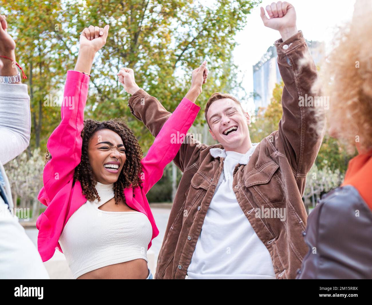 Eine Gruppe fröhlicher junger, multiethnischer männlicher und weiblicher Freunde in stilvollen Kleidern, die hell lächeln, während sie auf der Straße der Stadt mit den Fäusten auf der sonnigen d stehen Stockfoto