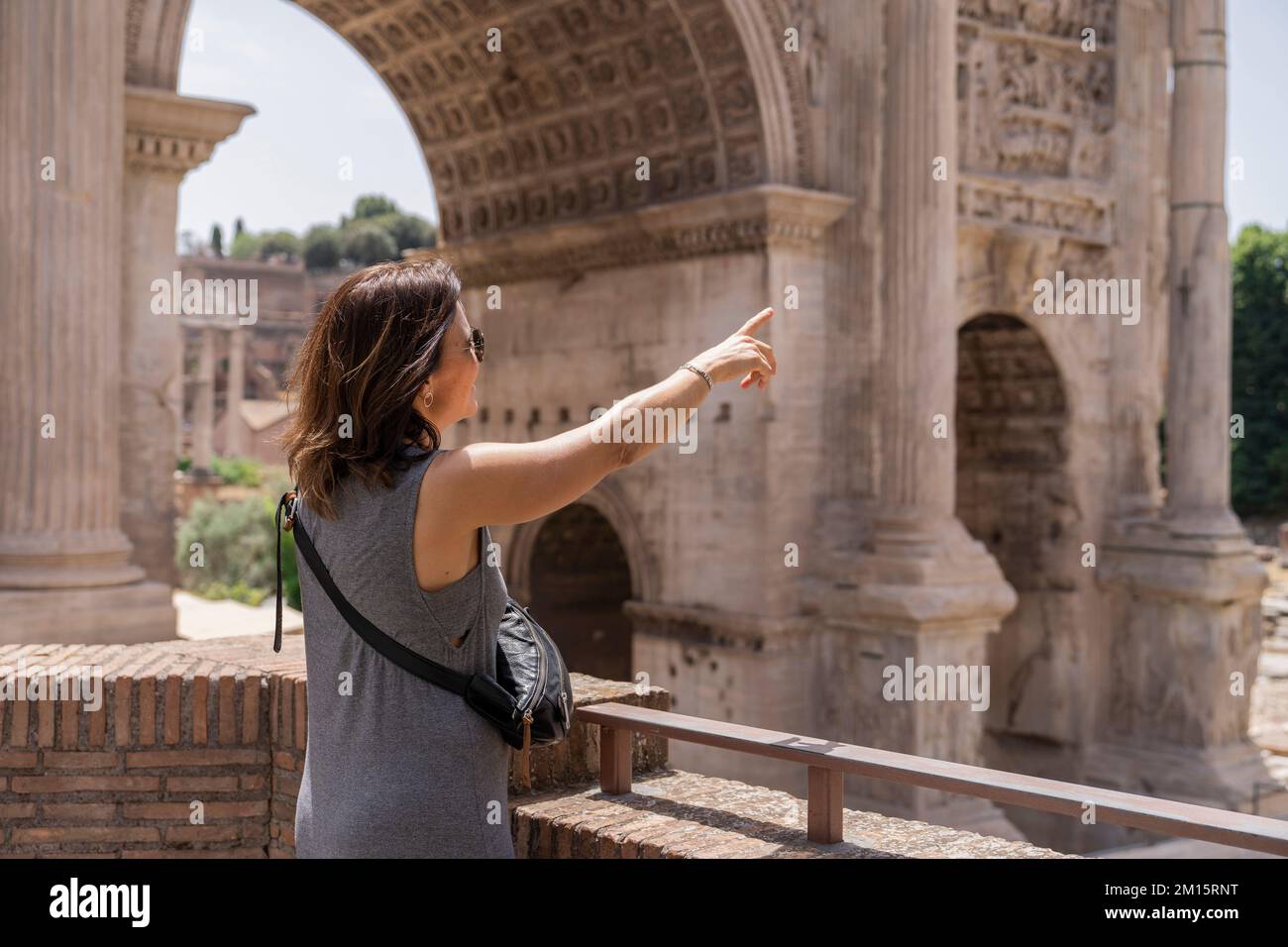 Rückansicht einer erwachsenen Frau in grauem Kleid, die neben dem Zaun vor dem berühmten Kolosseum in der Straße von Rom, Italien, steht Stockfoto