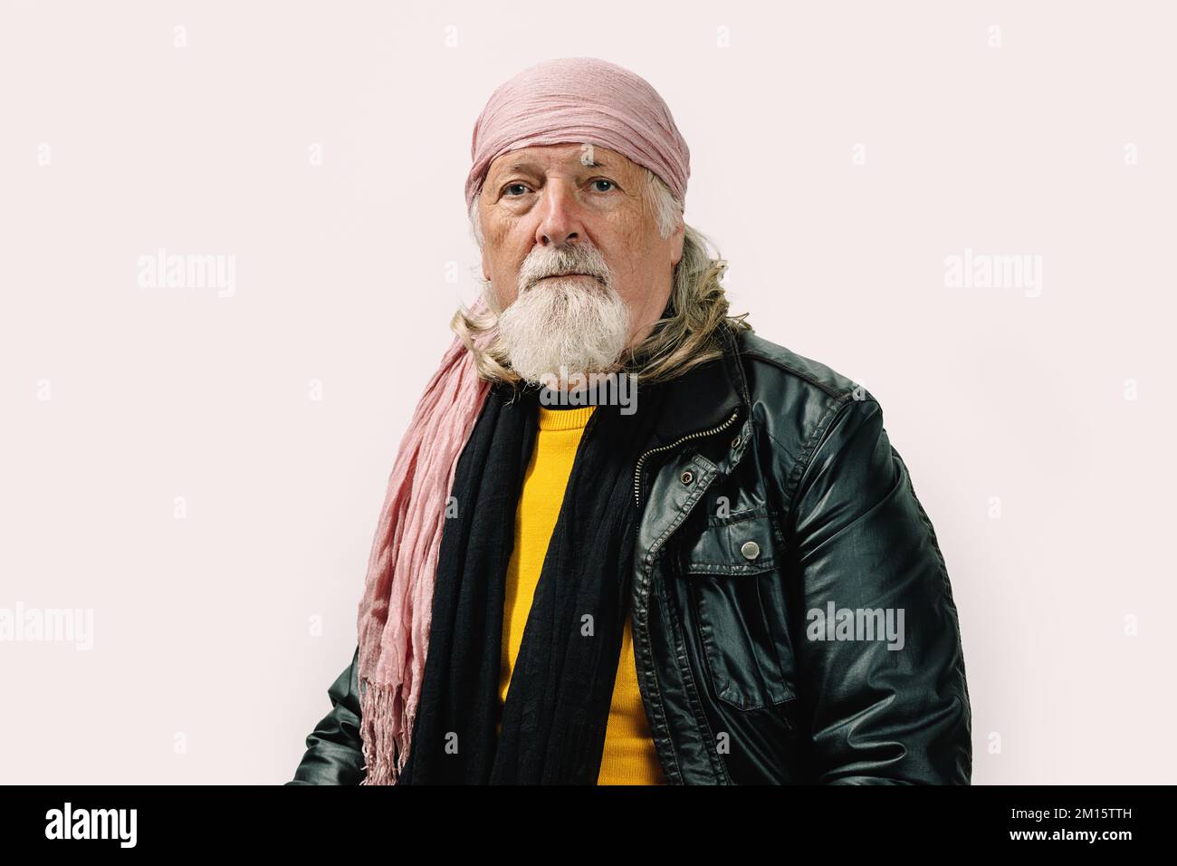 Ein bärtiger Senior-Mann in Lederjacke und Bandana, der vor weißem Hintergrund auf die Kamera schaut Stockfoto