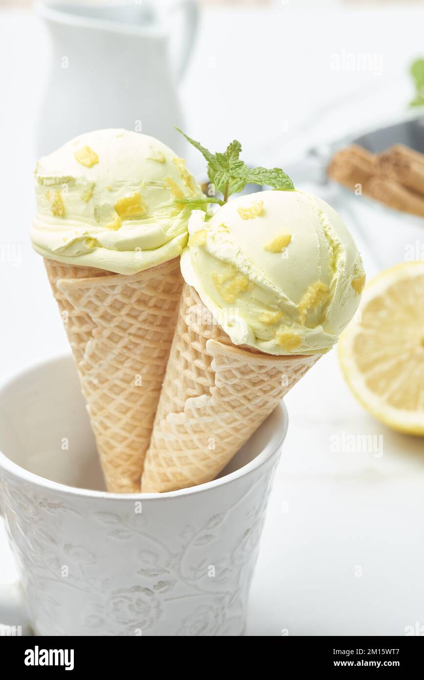 Ein Paar leckeres hausgemachtes Zitroneneis in knusprigen Waffelmuscheln, dekoriert mit Zest und Minzeblätter, die in den Becher auf dem Tisch in der Küche gelegt wurden Stockfoto