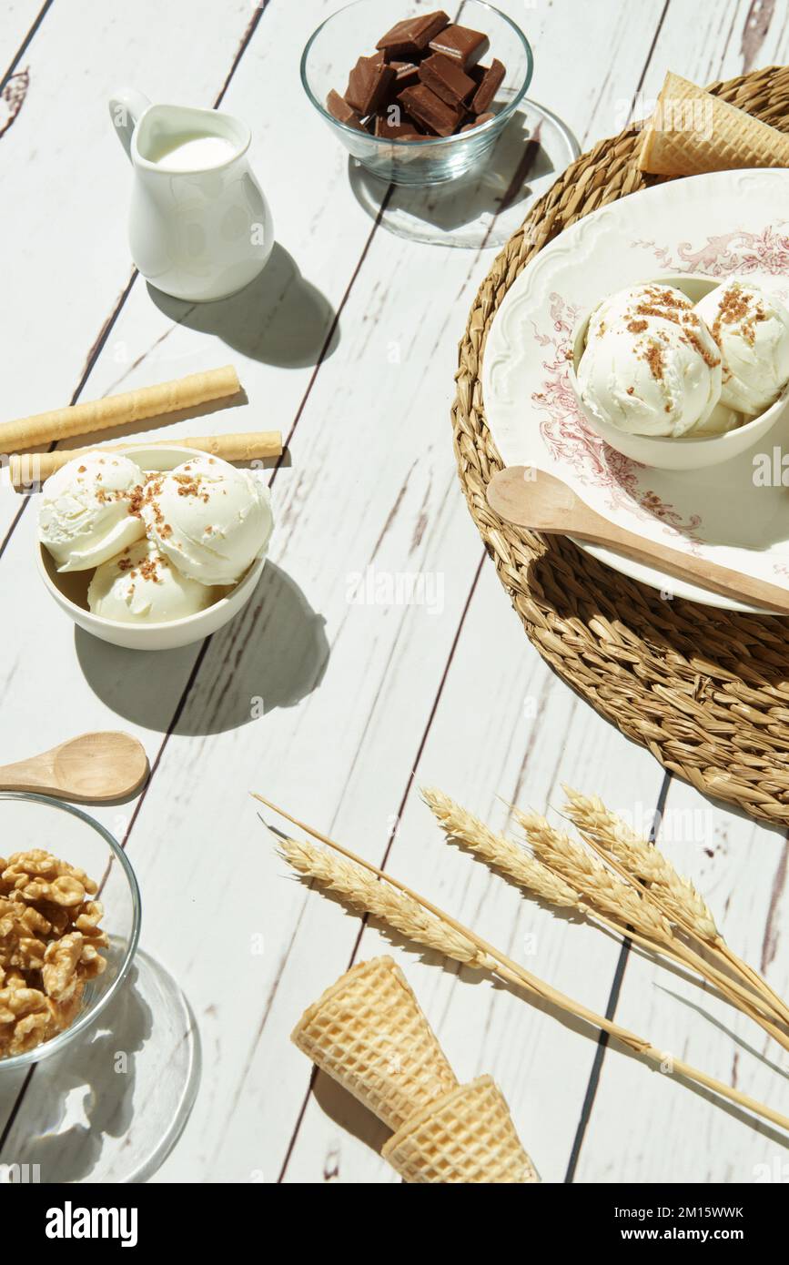 Von oben köstliches Eis, serviert in Schüsseln mit Waffelrollen und Zapfen und auf einem weißen Holztisch neben dem Krug mit Milch-Schokolade-Riegeln A Stockfoto