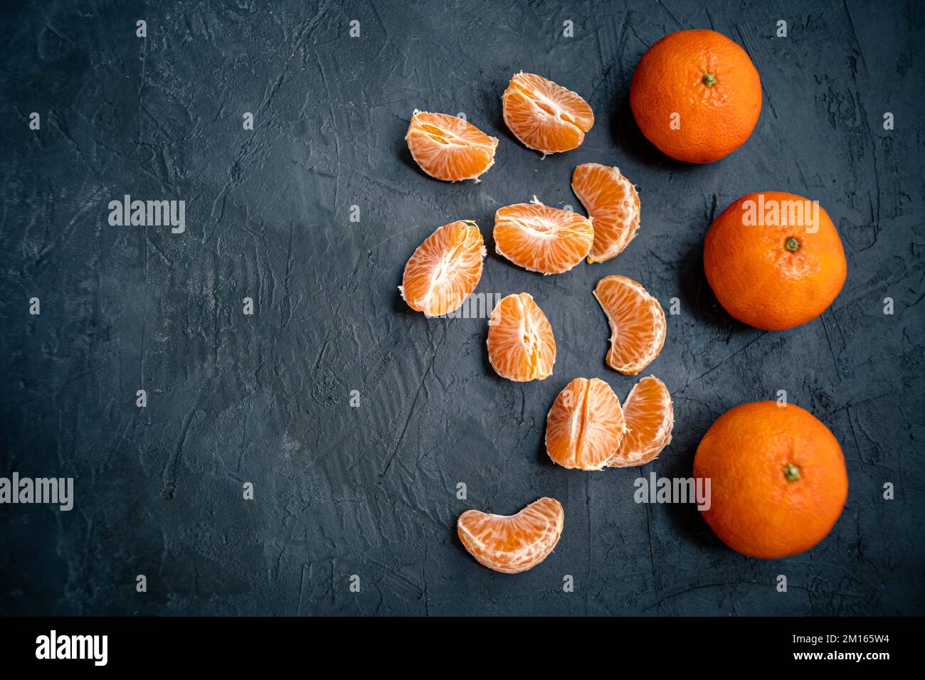 Mandarinenvollfrucht und Scheiben isoliert auf dunklem Schieferhintergrund. Ansicht von oben mit Kopierbereich für Text Stockfoto