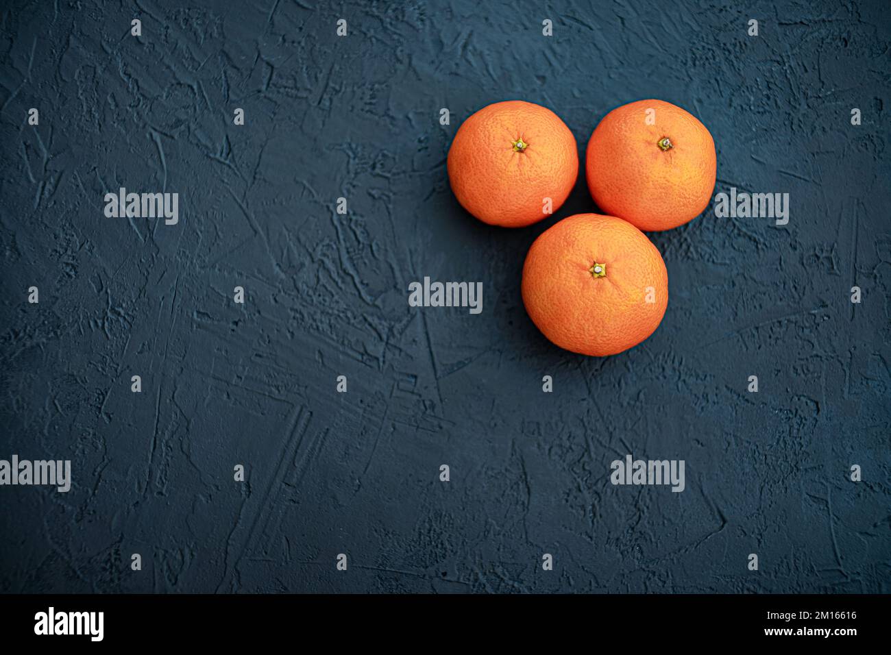 Drei isolierte Mandarinenfrüchte auf dunklem Schieferhintergrund. Ansicht von oben mit Kopierbereich für Text Stockfoto