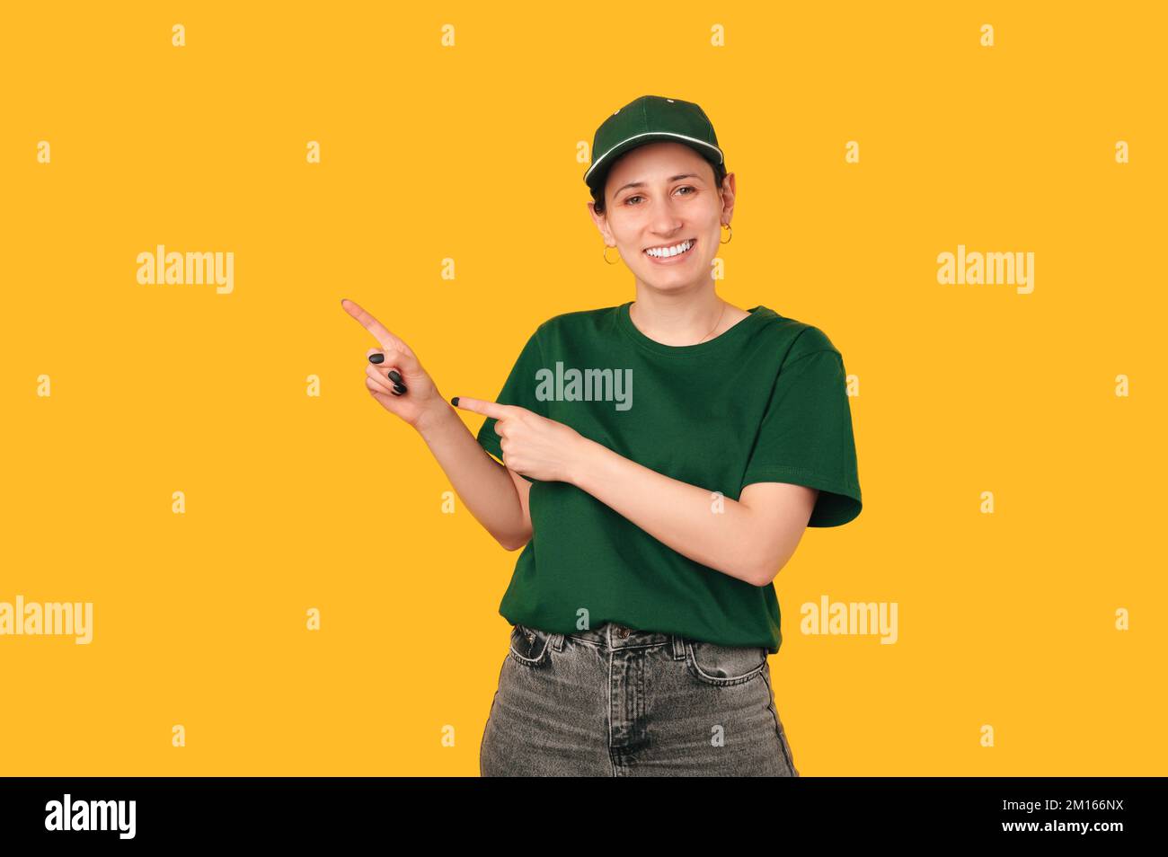 Fröhliche junge Frau, die die Uniform trägt, mit zwei Fingern auf gelbem Hintergrund. Stockfoto