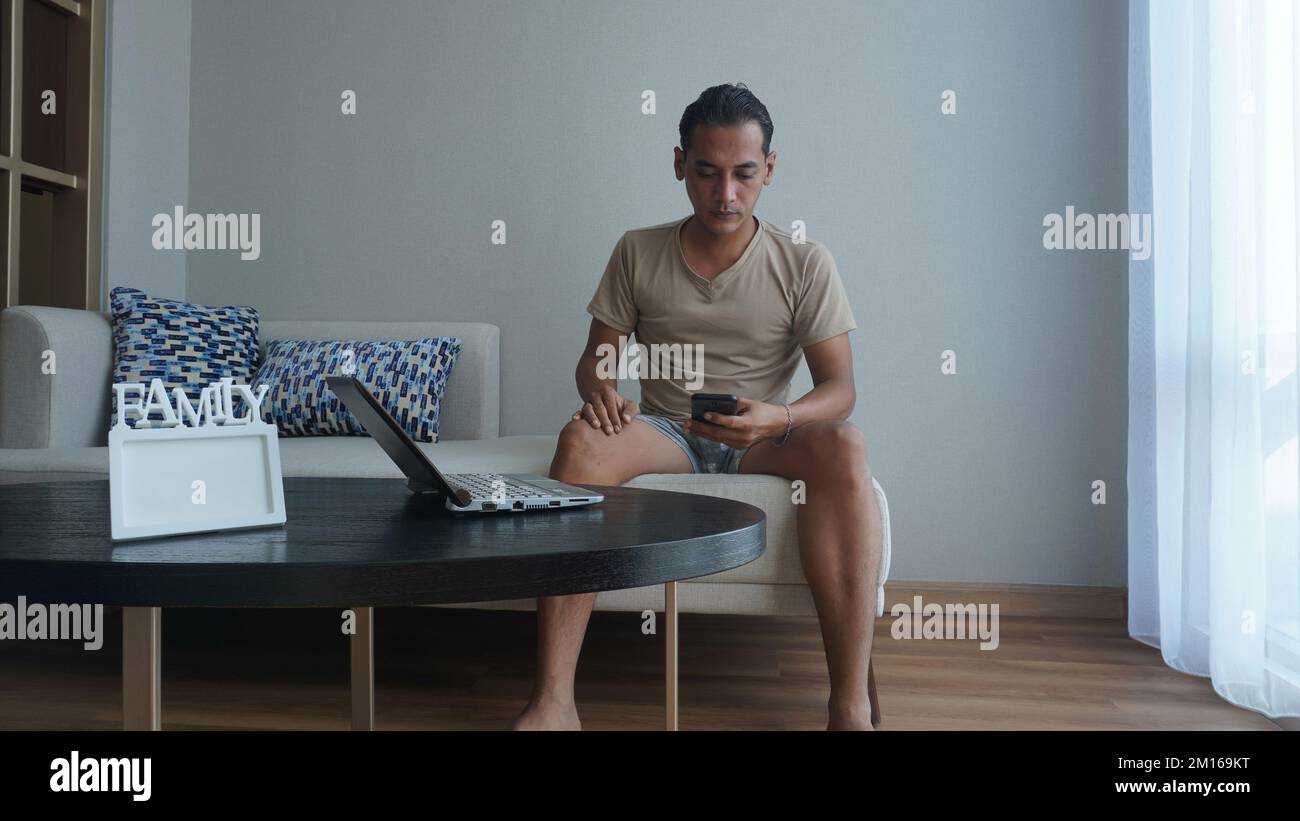 Concept Idea Design Interieur Wohnzimmer als Arbeitsplatz zu Hause. Mann, der von zu Hause aus mit Smartphone und Notebook arbeitet Stockfoto
