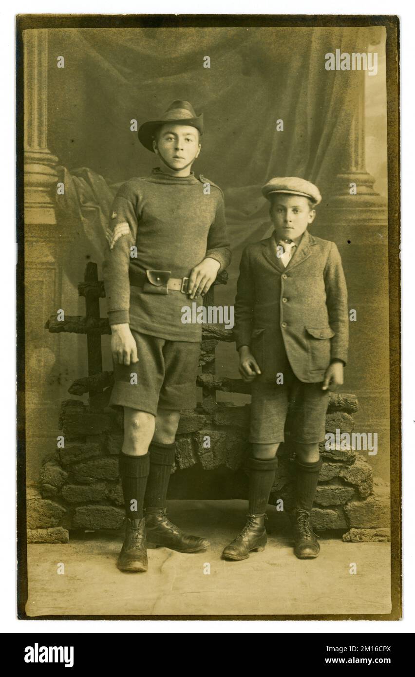 Die originale Postkarte von zwei Brüdern der Arbeiterklasse Anfang der 1920er Jahre – der älteste, ein Teenager – trägt die Uniform des Royal Marines Volunteer Cadet Corps (ehemals Royal Marines Artillery Cadet Corps bis in die 1910er Jahre). Die 3 Chevrons und eine Krone auf seinem Ärmel bezeichnen ihn als Kadett-Farbenfeldwebel. Er steht neben seinem jüngeren Bruder. Beide Jungs tragen kurze Hosen und Stiefel, der jüngste eine Jacke und eine flache Mütze. In den frühen 1920er Jahren wurden kurze Hosen und lange Socken für Jungen normal und sie trugen sie bis zum Alter von 13 Jahren und die Mode ging bis in die 1960er Jahre weiter. GROSSBRITANNIEN Stockfoto