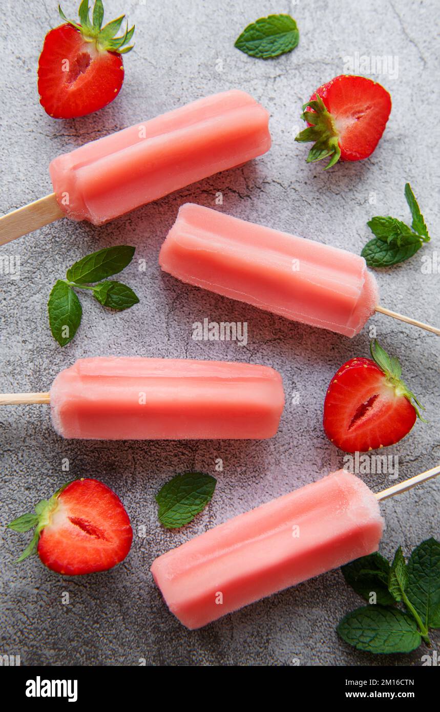 Hausgemachte gefrorene Erdbeer-Eis-Eiszapfen und frische Erdbeeren auf einem betonierten Hintergrund. Sommerdessert Stockfoto